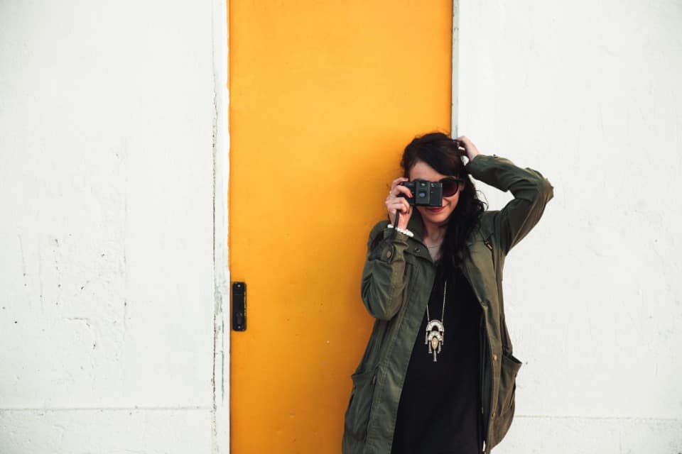 A young creator taking a photo, standing against a yellow door